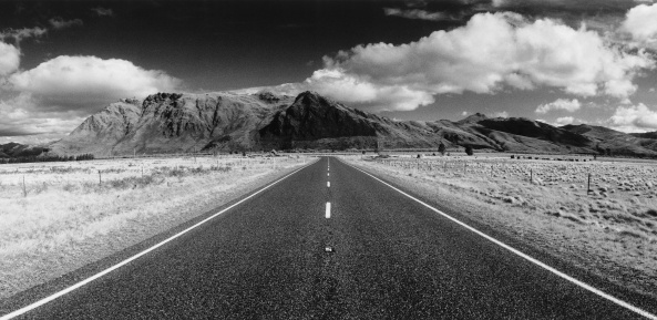A grayscale view of the open countryside road with mountains and grasses