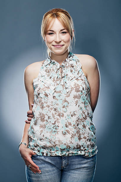 Young smiling woman in magenta pleated dress is posing with hands on hip and looking to the side. Three quarter length studio shot against yellow background.