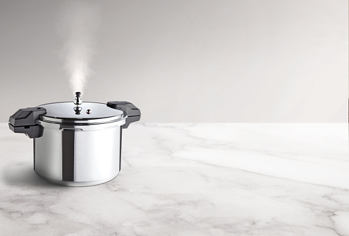 Pressure cooker with a steam coming out, on an empty marble countertop