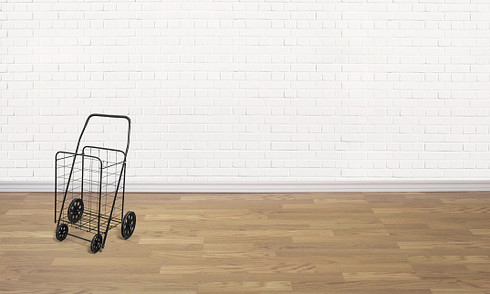 Empty black domestic shopping cart in an empty room with hardwood floors and brick white walls