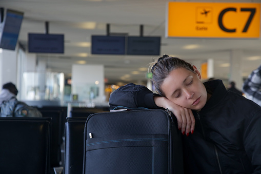 Tired tourist woman sleeping on luggage while waiting for her flight at the airport terminal