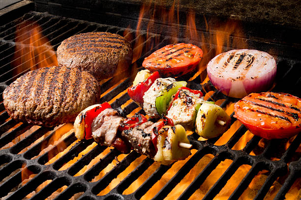 Chicken Shish Kebabs with bell pepper and grilled chicken breast and beef Grilled Burger, Tomato, Onion on a flaming old fashioned charcoal barbecue grill with perfect grill marks on everything