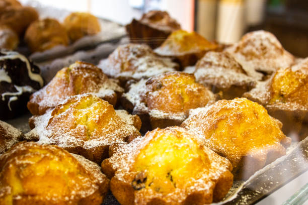 istock Cupcakes on display. Freshly baked cupcakes with powdered sugar behind a glass showcase in a cafe. 1551308477