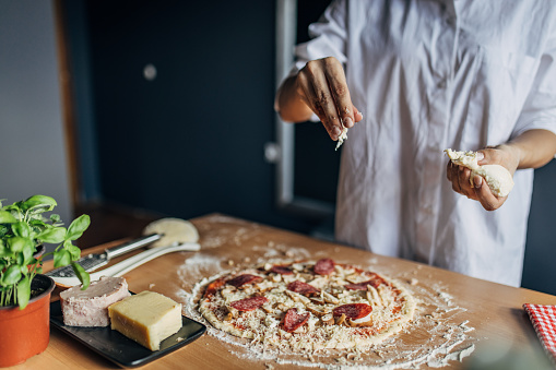 The woman puts mozzarella on the pizza dough. She prepares pizza at home, on the wooden table. Unrecognizable person.
