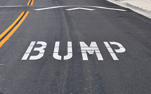White bump road marking on black tarmac The word bump spelled out on the street before a speed bump, which is also know as a sleeping policeman, kipping cop, slow child, road hump, speed hump, speed breaker, judder bar, or ramp. bumpy photos stock pictures, royalty-free photos & images