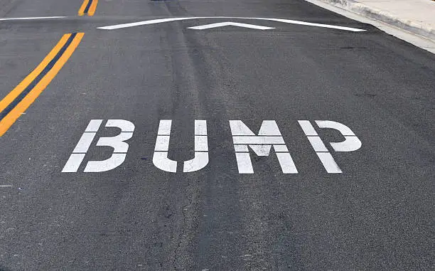 The word bump spelled out on the street before a speed bump, which is also know as a sleeping policeman, kipping cop, slow child, road hump, speed hump, speed breaker, judder bar, or ramp.