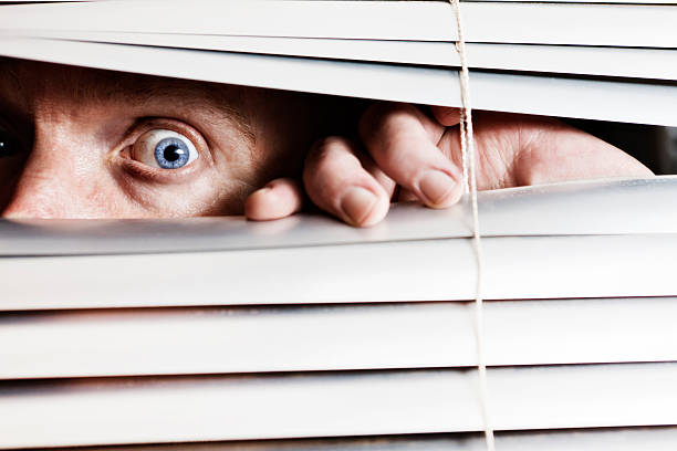 istock Terrified looking man looks, wide-eyed, through venetian blind 155132940