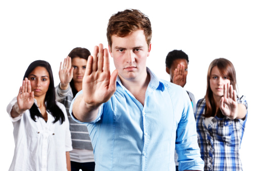 A mixed group of five young people look  determined as they hold their hands up indicating 