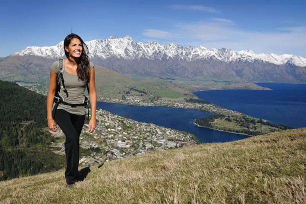 Beautiful woman in a sports outfit hiking in New Zealand. You can see a the famous city Queenstown and the Lake Wakatipu with the Remarkables Mountains in back. Nikon D3X. Converted from RAW.