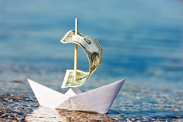 Paper boat with $1 bill sail is blown onshore  sinking stock pictures, royalty-free photos & images