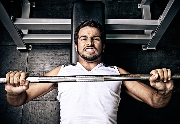Young man putting effort in on a bench press Man struggling on the bench press struggle stock pictures, royalty-free photos & images