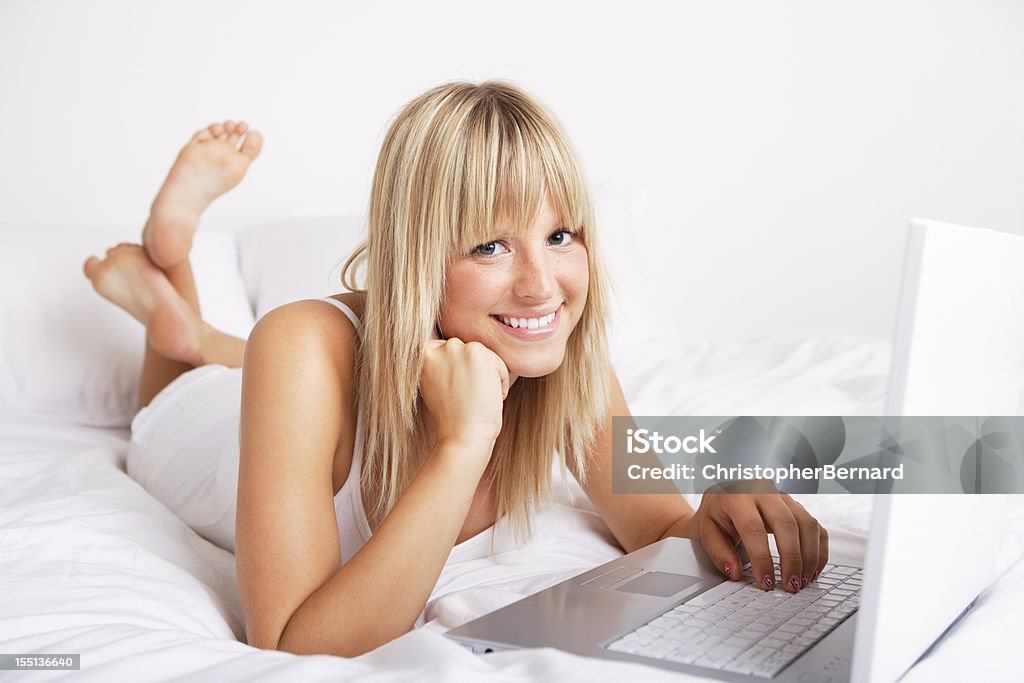 Mujer sonriente usando una computadora portátil en la cama - Foto de stock de Mujeres libre de derechos