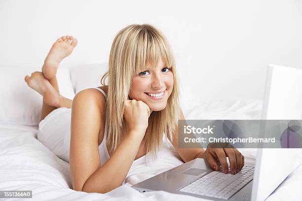 Mujer Sonriente Usando Una Computadora Portátil En La Cama Foto de stock y más banco de imágenes de Mujeres