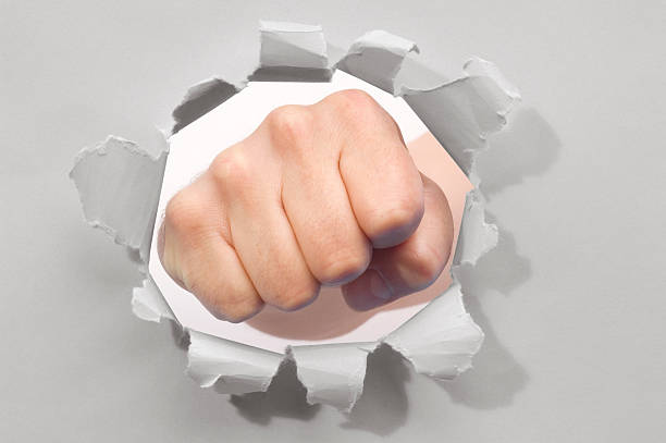 istock Fist punching through a ripped hole in a paper 155136682