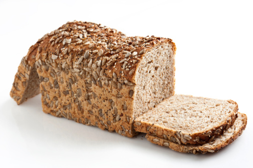 Whole grain rye bread with seeds cut into bread slices on wooden board, top view