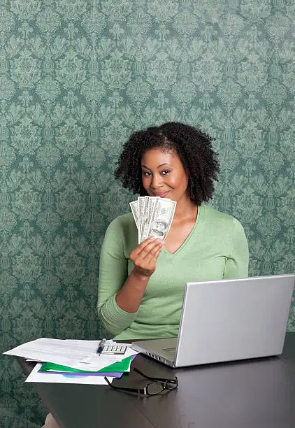 Portrait of  woman holding currency while using laptop at home