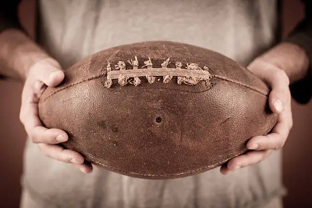 Close up color photo of a vintage football player holding an old football. Some desaturation and grain added for vintage feel.