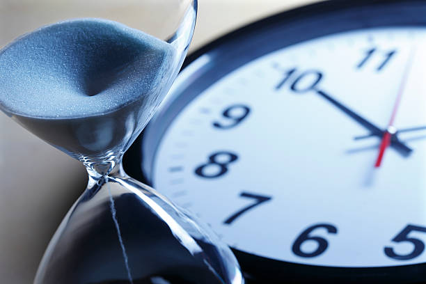 istock Sand pouring through an hourglass in front of clock 155137782