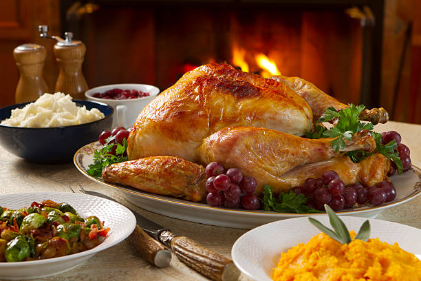 Freshly roasted turkey dinner with vegetables in bowls Holiday dinner with roast turkey, butternut squash, Brussels sprout, mashed potatoes, and cranberry sauce, all served by a roaring fire. carving set stock pictures, royalty-free photos & images