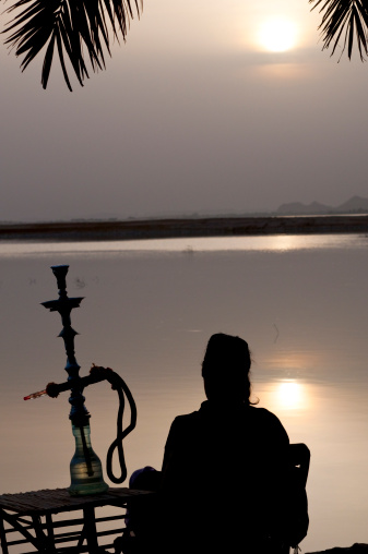 A woman sits beside Lake Siwa and watches the landscape and setting sun. Located a few kilometers away from the town of Siwa in Egypt, the lake is surrounded by the vast Western Desert.