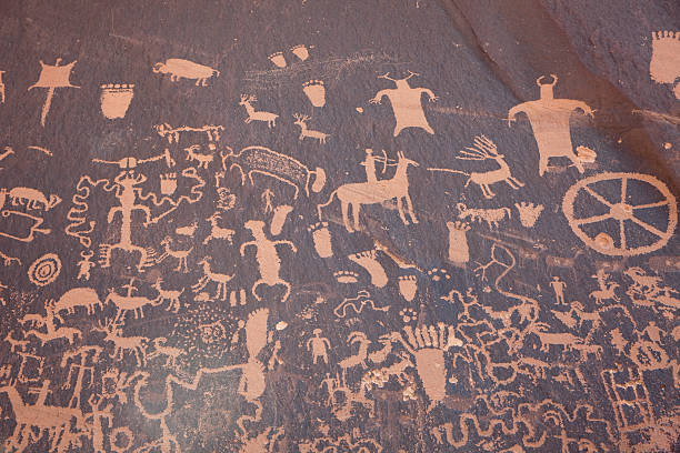 Panel of Native American Newspaper Rock petroglyphs Utah horizontal Just outside Canyonlands National Park in Utah, the massive wall of Native American petroglyphs panel known as Newspaper Rock State Historic Monument. The petroglyphs are from the Archaic, Basketmaker, Fremont, and Pueblo cultures who farmed the Puerco River Valley 650 to 2,000 years ago and show a variety of animals, symbols, footprints, hunting scenes and more. cave painting stock pictures, royalty-free photos & images