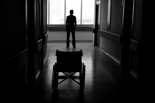 Silhouette of man leaving wheelchair in corridor of hospital.The image was taken in real hospital.Light at the end of corridor is visible for symbolic purpose.Black and white tone is used for effective atmosphere.Photo was shot with DSLR camera.