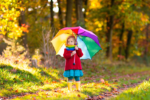 Kid playing out in the rain. Children with umbrella and rain boots play outdoors in heavy autumn rain. Little girl jumping in muddy puddle. Kids fun by rainy fall weather. Child running in storm.