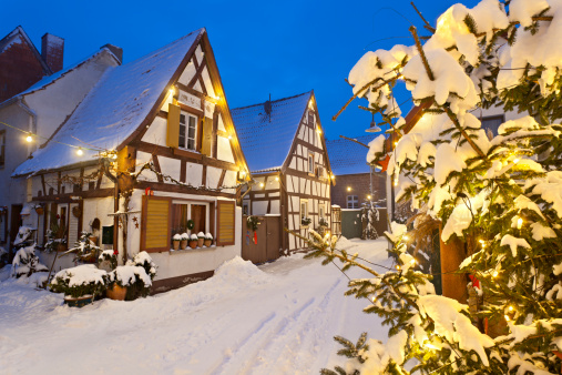 An old village street with half-timbered houses and christmas lights at night during snowfall.
