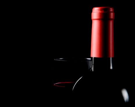 Silhouettes of a red wine bottle with red foil and a glass of red wine with a whisper of red wine visible