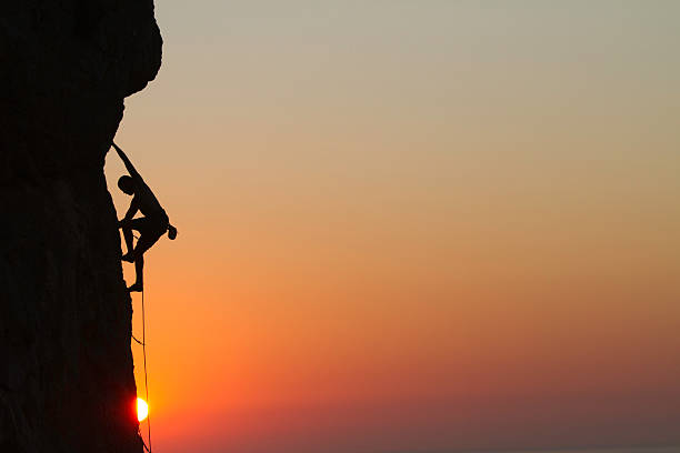 Silhouette of a man rock climbing at sunset stock photo