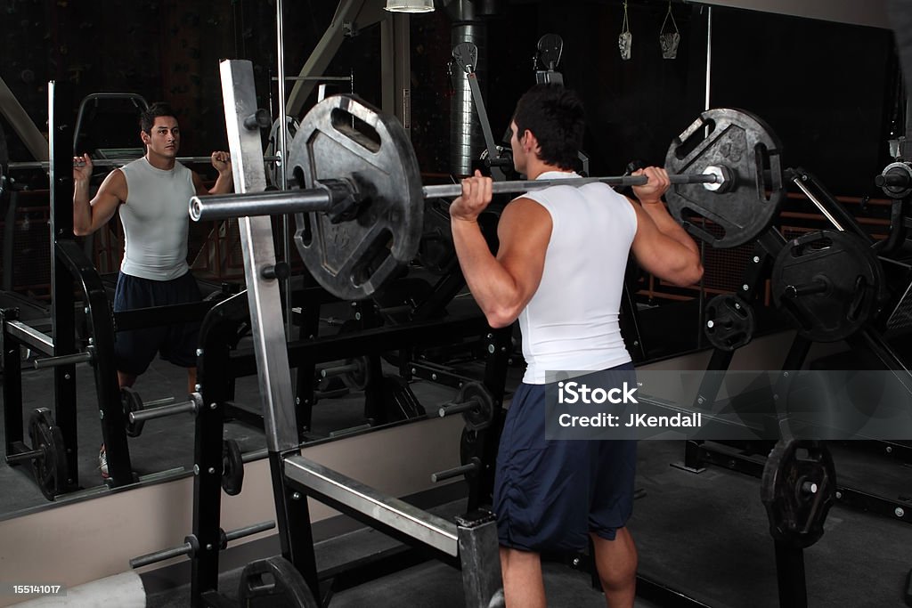 Masculino jovem muscular levantando pesos em frente do espelho - Royalty-free Agachar-se Foto de stock