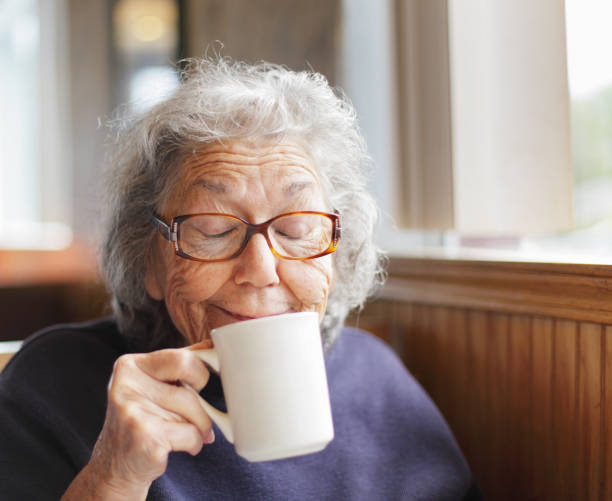 Senior Woman Funny Face Smile With Coffee Cup A senior woman is making a funny face smile as she drinks from her coffee cup in a restaurant. Shallow depth of field. only senior women stock pictures, royalty-free photos & images