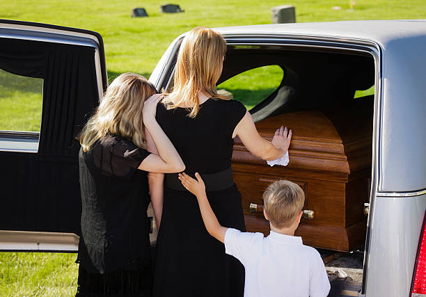Grieving Family at a Funeral A woman and two children standing behind an open hearse. child casket stock pictures, royalty-free photos & images
