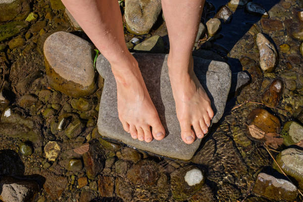 istock Close up of human feet standing on river rock surrounded by river 1551420233