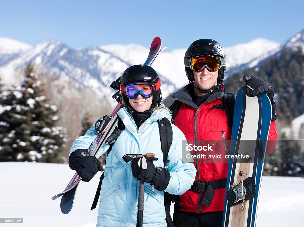 Skier Couple Portrait Portrait of an attractive young couple carrying downhill skis and a snowboard outside in the mountains which are covered in snow. 20-24 Years Stock Photo