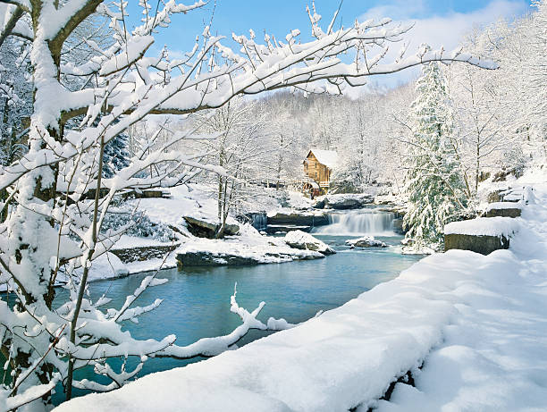 nostalgic gristmill in snowy winter country scene A fresh blanket of snow on a nostalgic old-fashioned gristmill and stream in a pubic state park. snow river stock pictures, royalty-free photos & images