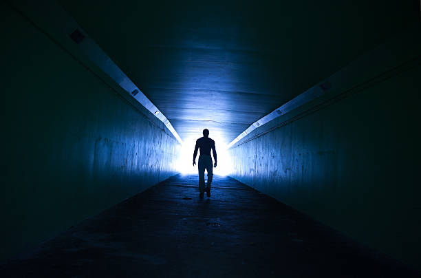 Lone man walking through tunnel Silhouetted with a blue tone for effect light at the end of the tunnel stock pictures, royalty-free photos & images