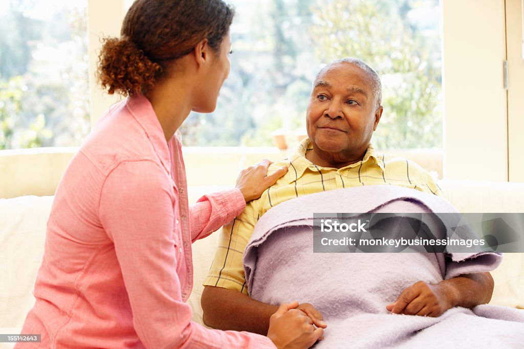 Daughter tending to her sick father Woman looking after sick father at home in the living room Senior Adult Stock Photo