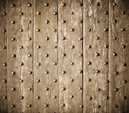 Close-up of a heavily weathered antique wooden surface, studded with metal rivets.