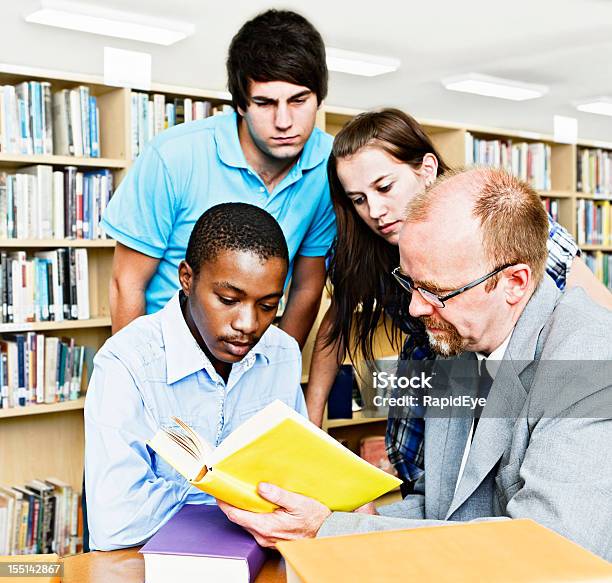 Foto de Três Alunos E Professor Estudo Um Livro Na Biblioteca De Campus e mais fotos de stock de 20 Anos