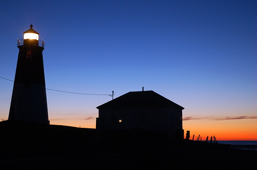 The beacon of the Point Judith Lighthouse shines as the sky behind it brightens at sunrise