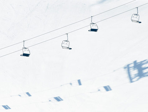 Photographed from above, an empty chairlift casting shadows onto the snow of a ski piste.