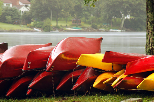 A large number of yellow and red canoes are piled on top of each other at a lake for a summer camp