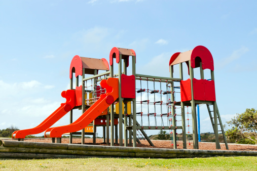 Red playground equipment with slides and ladders against blue sky, full frame horizontal composition with copy space