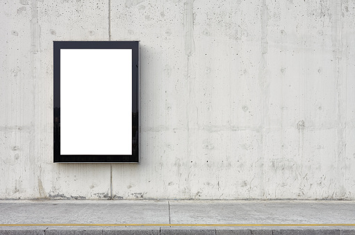 Blank billboard on wall. Wall is made of concrete and gray coloured. Billboard is oriented vertically and standing on the left side of frame. Edges of billboard are black. Billboard is empty so you can write or add something on it. - Clipping path of billboard included.