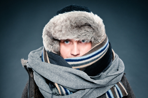 Handsome man in winter clothes, very warm and thickly clothed. He has two scarves, thick warm fur cap.
