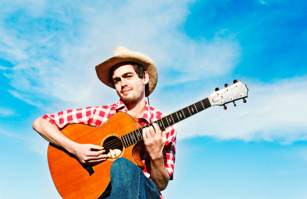 istock Happy country boy sits strumming his guitar smiling 155144096