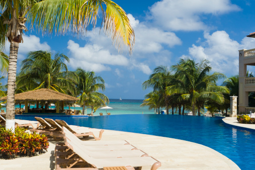 Resort infinity pool overlooks tropical beach, palm trees, and Caribbean Sea. Roatan, Honduras