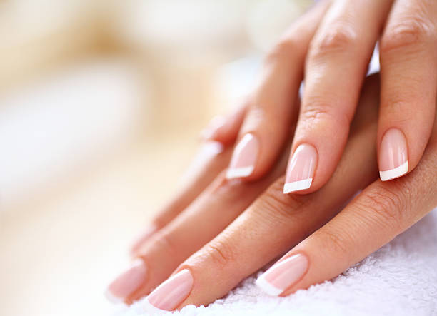 Manicure. Closeup of nicely manicured female fingernails. One hand is placed on top of other, both on a white towel. Very nice french manicure with transparent nail paint. Blurry beige background. Copy space. body care and beauty photos stock pictures, royalty-free photos & images