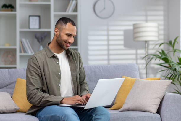 istock A young smiling African-American man is sitting on a sofa and using a laptop, spending free time on the Internet, chatting 1551445995